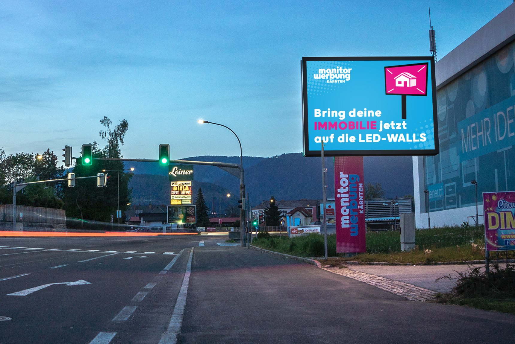 Eine LED-Wall neben der Straße am Abend fotografiert. Darauf eine Grafik mit dem TItel "Bring deine Immobilie auf die LED-Walls"