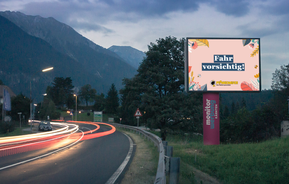 LED Wall neben der Straße bei Nacht, mot der Grafik "Fahr vorsichtig"